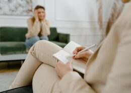 A professional coach taking notes during a session with a client sitting in the background, symbolizing structured coaching packages and personalized client support for transformation and success.