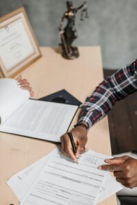A person signing documents on a wooden desk with a certificate and pen holder in the background, symbolizing professionalism and certification for Life coach certification