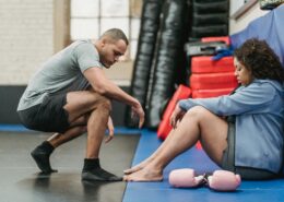 Health and wellness coach supporting a woman during a workout session, offering encouragement and mindset support in a gym setting.