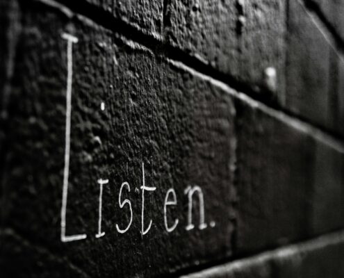 Word 'Listen' written on a dark brick wall, symbolizing the power of active listening in coaching to build trust and transformation.