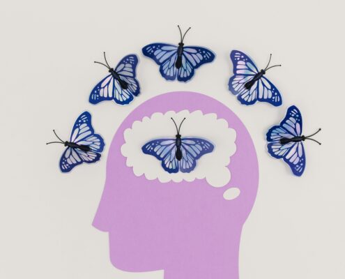Creative coaching with art therapy concept showing blue butterflies emerging from a paper-cut human mind, symbolizing emotional expression and personal transformation.