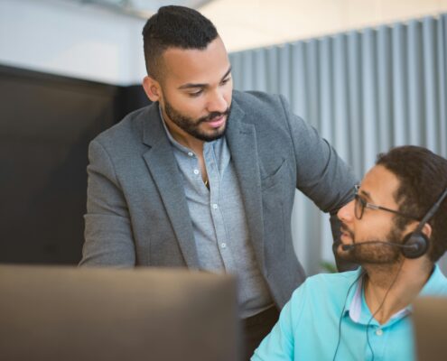 Manager providing employee performance coaching to support team member at desk in modern office.