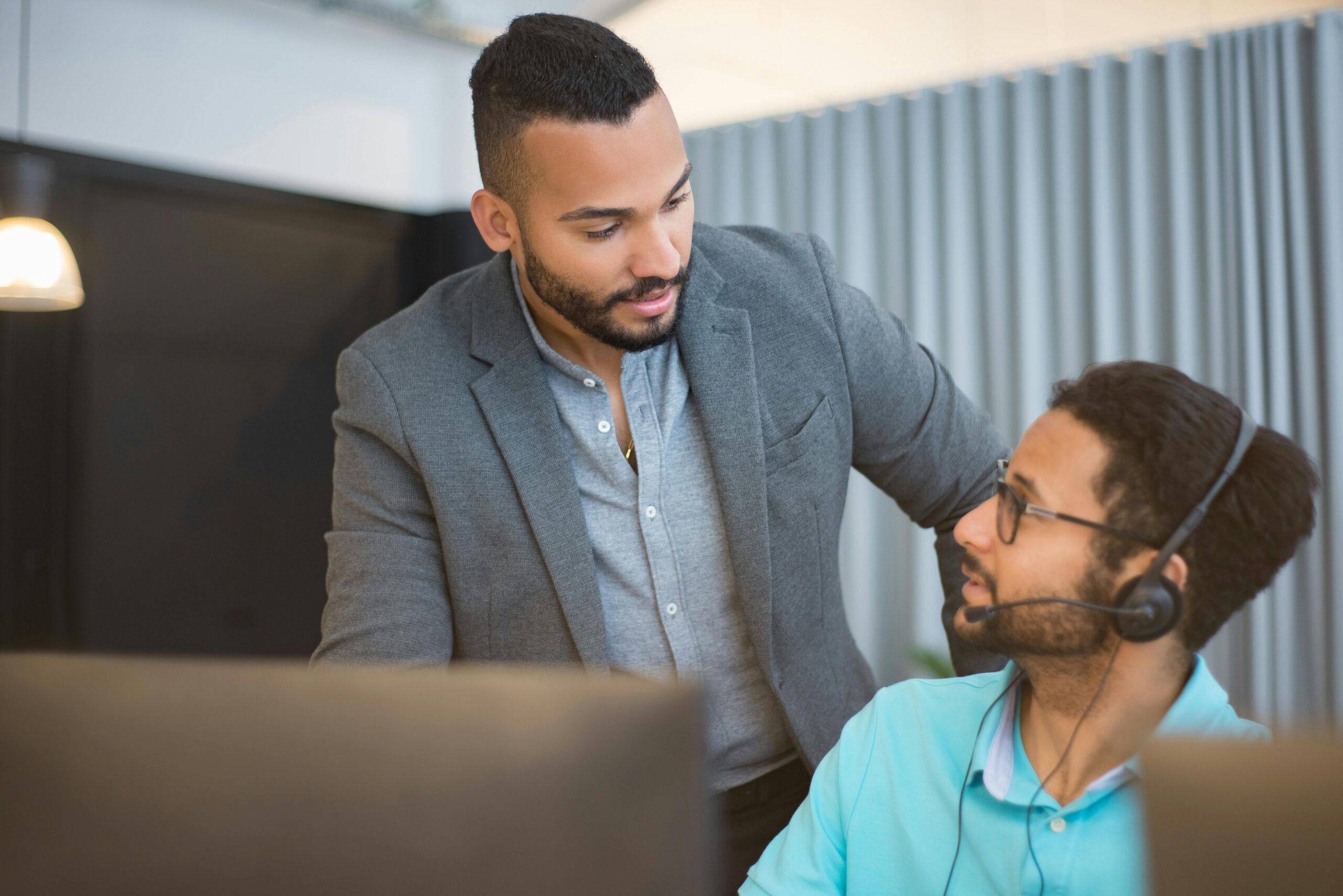 Manager providing employee performance coaching to support team member at desk in modern office.