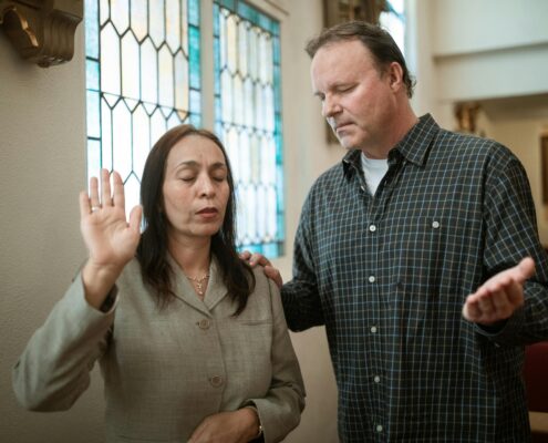 Forgiveness coaching session with a woman practicing emotional release while a supportive coach stands beside her in a peaceful church setting