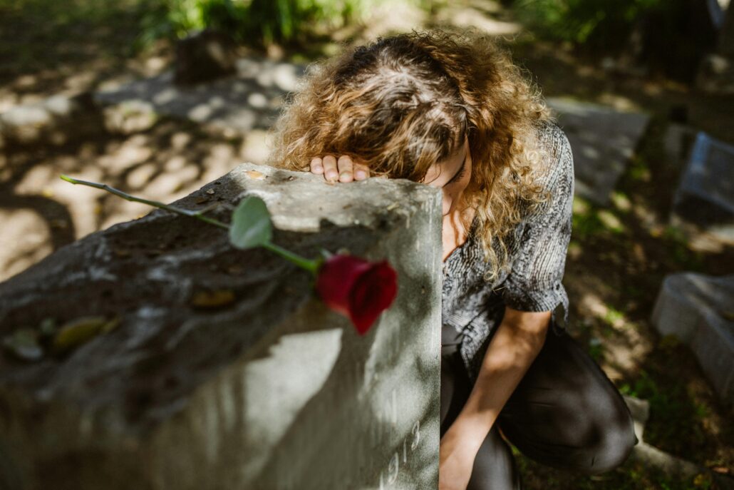 Woman grieving at a gravesite with a red rose, representing grief coaching techniques for coaches supporting clients through loss