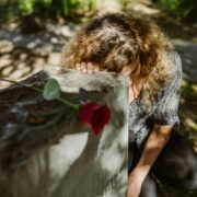 Woman grieving at a gravesite with a red rose, representing grief coaching techniques for coaches supporting clients through loss