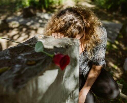 Woman grieving at a gravesite with a red rose, representing grief coaching techniques for coaches supporting clients through loss