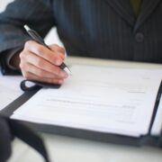 Person signing official documents about life coach licensing requirements and certification