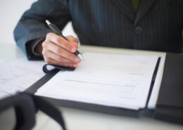 Person signing official documents about life coach licensing requirements and certification