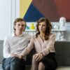 A well-dressed couple sitting close together on a sofa in a modern living room, looking calm and connected—illustrating couples coaching vs couples therapy and the different approaches to strengthening relationships.