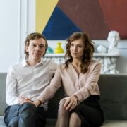 A well-dressed couple sitting close together on a sofa in a modern living room, looking calm and connected—illustrating couples coaching vs couples therapy and the different approaches to strengthening relationships.