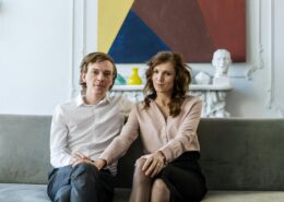 A well-dressed couple sitting close together on a sofa in a modern living room, looking calm and connected—illustrating couples coaching vs couples therapy and the different approaches to strengthening relationships.