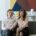 A well-dressed couple sitting close together on a sofa in a modern living room, looking calm and connected—illustrating couples coaching vs couples therapy and the different approaches to strengthening relationships.