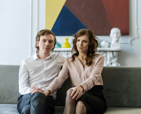 A well-dressed couple sitting close together on a sofa in a modern living room, looking calm and connected—illustrating couples coaching vs couples therapy and the different approaches to strengthening relationships.