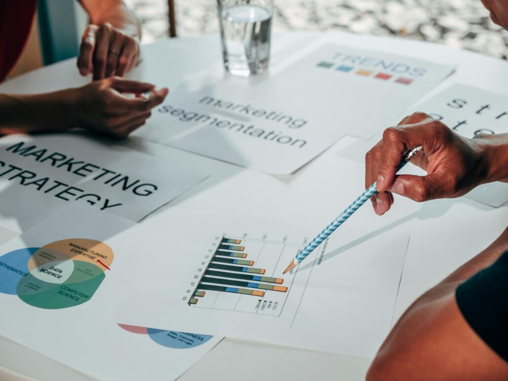 Hands pointing at marketing charts and strategy documents on a table during a collaborative planning session, illustrating a coaching lead magnet focused on attracting and engaging ideal clients.