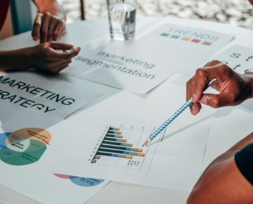 Hands pointing at marketing charts and strategy documents on a table during a collaborative planning session, illustrating a coaching lead magnet focused on attracting and engaging ideal clients.