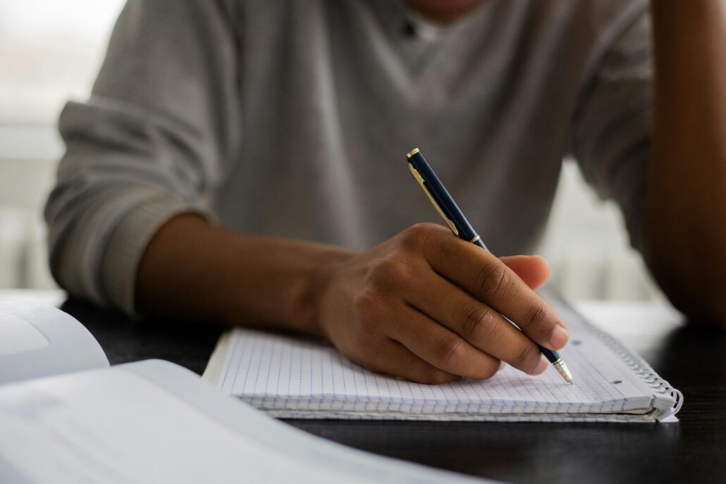Person writing notes in a notebook during a coaching session, illustrating the process of creating a coaching bio and reflecting on professional experience, skills, and personal values.