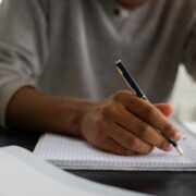 Person writing notes in a notebook during a coaching session, illustrating the process of creating a coaching bio and reflecting on professional experience, skills, and personal values.