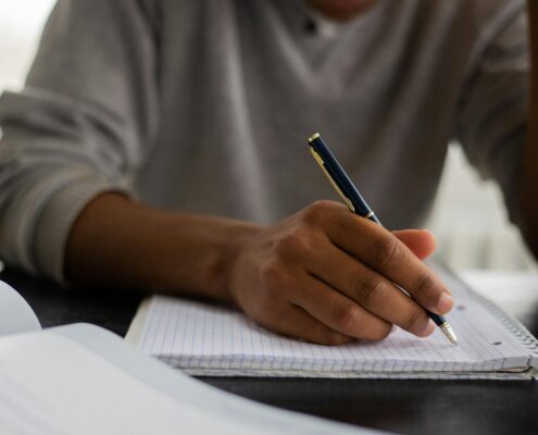 Person writing notes in a notebook during a coaching session, illustrating the process of creating a coaching bio and reflecting on professional experience, skills, and personal values.