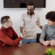 Professional coaching men in a collaborative workplace setting, with three colleagues engaged in discussion and a handshake during a team meeting.