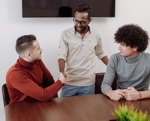Professional coaching men in a collaborative workplace setting, with three colleagues engaged in discussion and a handshake during a team meeting.
