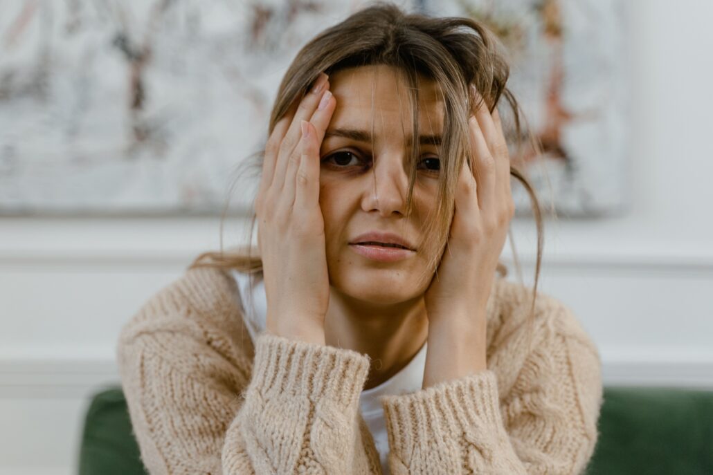 Woman holding her head with a distressed expression, illustrating the emotional impact addressed through trauma-informed coaching.