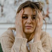 Woman holding her head with a distressed expression, illustrating the emotional impact addressed through trauma-informed coaching.