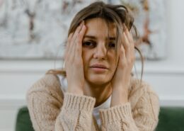 Woman holding her head with a distressed expression, illustrating the emotional impact addressed through trauma-informed coaching.