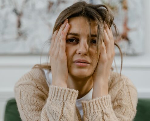 Woman holding her head with a distressed expression, illustrating the emotional impact addressed through trauma-informed coaching.