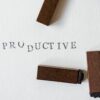 Wooden letter stamps arranged around the word “PRODUCTIVE” printed on white textured paper, symbolizing focus, organization, and productivity coaching.