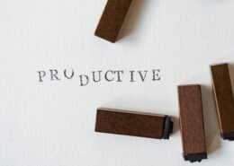 Wooden letter stamps arranged around the word “PRODUCTIVE” printed on white textured paper, symbolizing focus, organization, and productivity coaching.