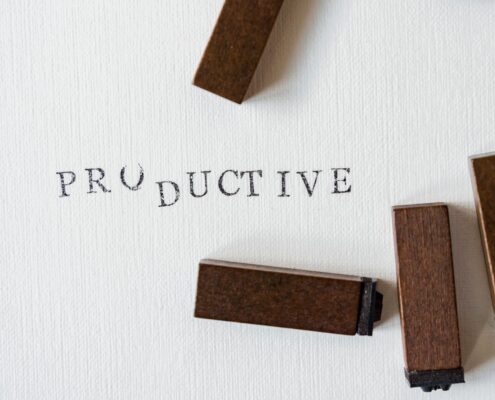 Wooden letter stamps arranged around the word “PRODUCTIVE” printed on white textured paper, symbolizing focus, organization, and productivity coaching.