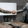Corporate coaching professionals shaking hands during a business meeting in a modern conference room.