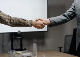 Corporate coaching professionals shaking hands during a business meeting in a modern conference room.