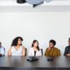 A diverse group of professionals participating in workshops to get coaching clients, seated together around a conference table during a collaborative business discussion.