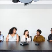 A diverse group of professionals participating in workshops to get coaching clients, seated together around a conference table during a collaborative business discussion.