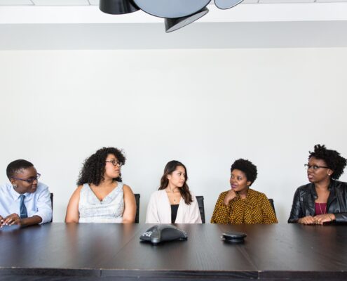 A diverse group of professionals participating in workshops to get coaching clients, seated together around a conference table during a collaborative business discussion.